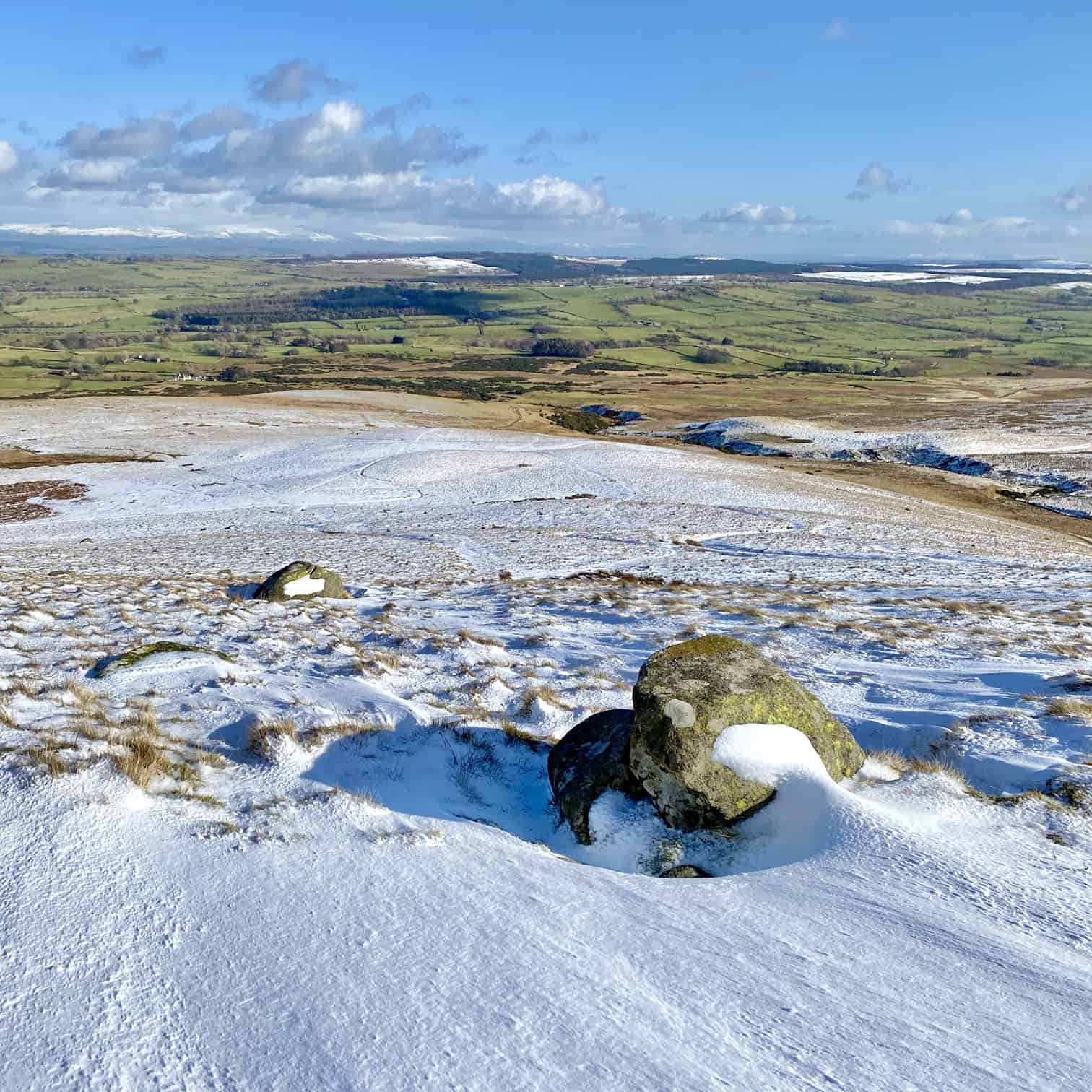 The view east from West Fell. On the horizon on the left of the photo the snow-covered mountains of the North Pennines are lit up by the sun.