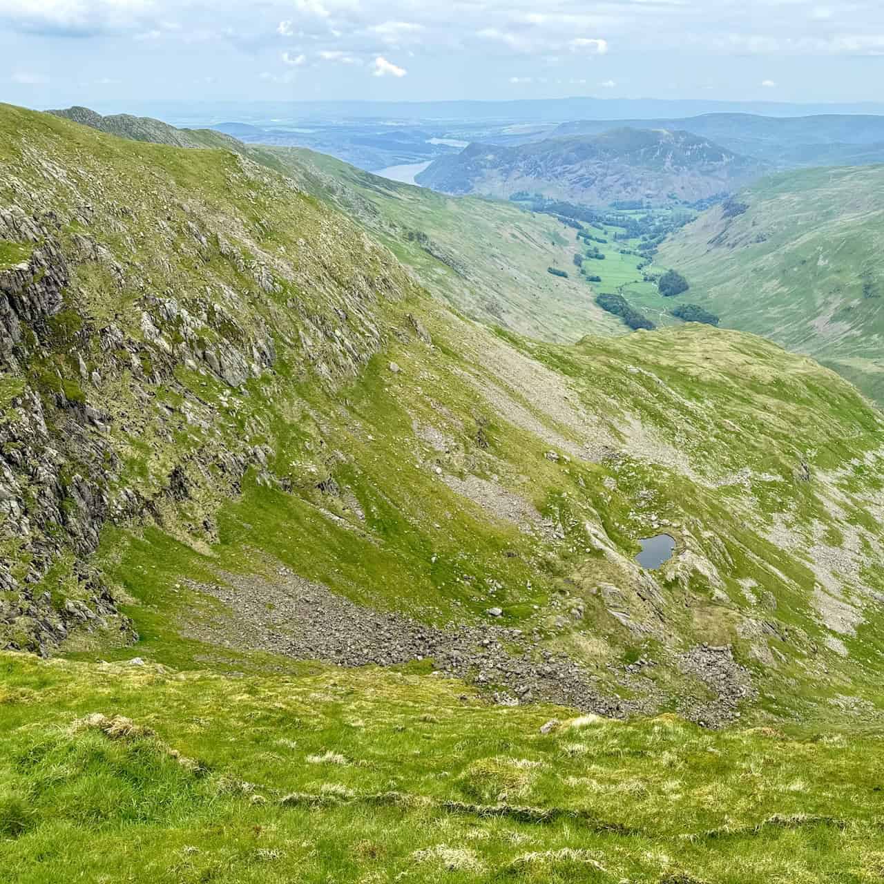 From High Crag, we observe the rocky slopes of Nethermost Crag on the left, with Hard Tarn below. Place Fell and Ullswater are visible in the distance.