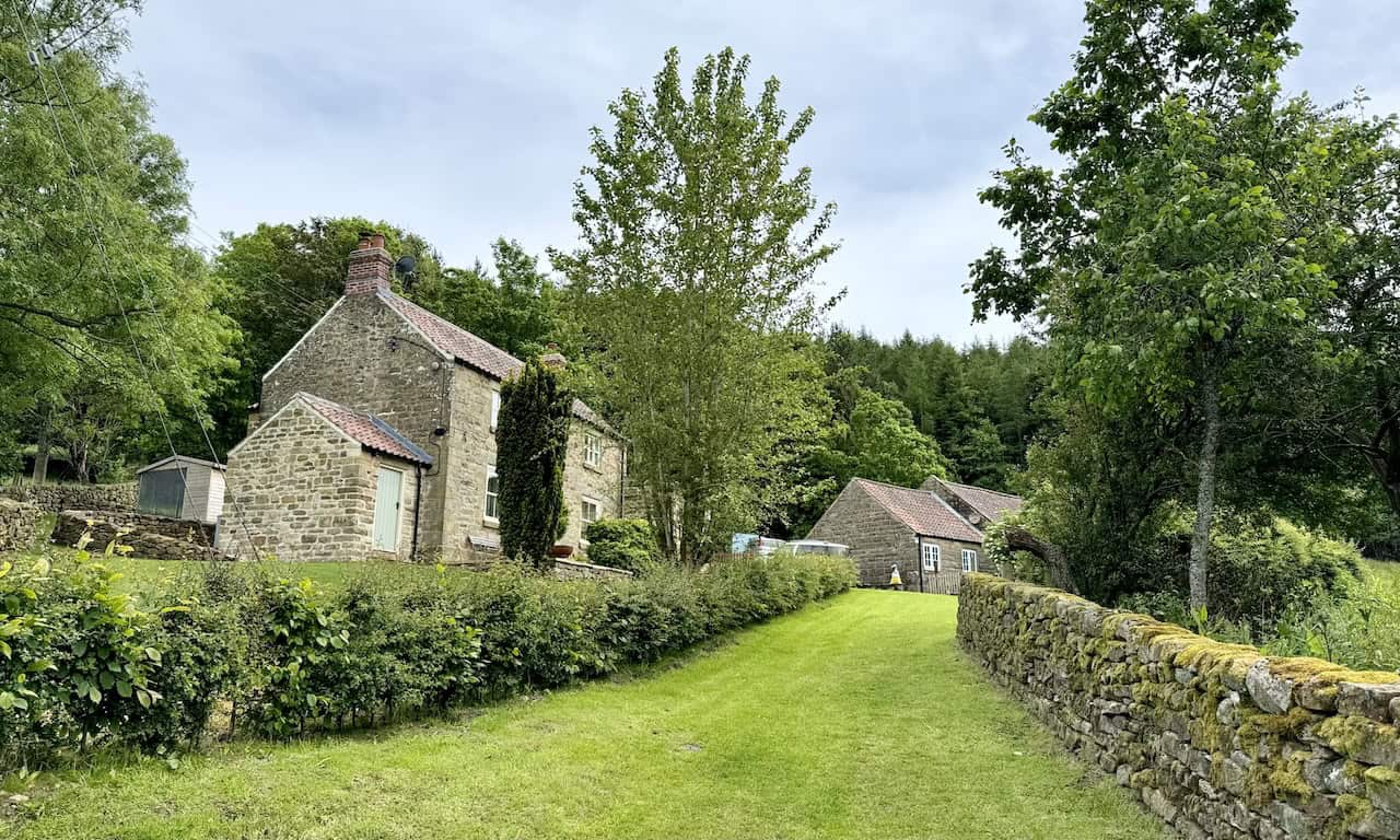 Picturesque route through Hagg End Farm with well-kept buildings and gardens.
