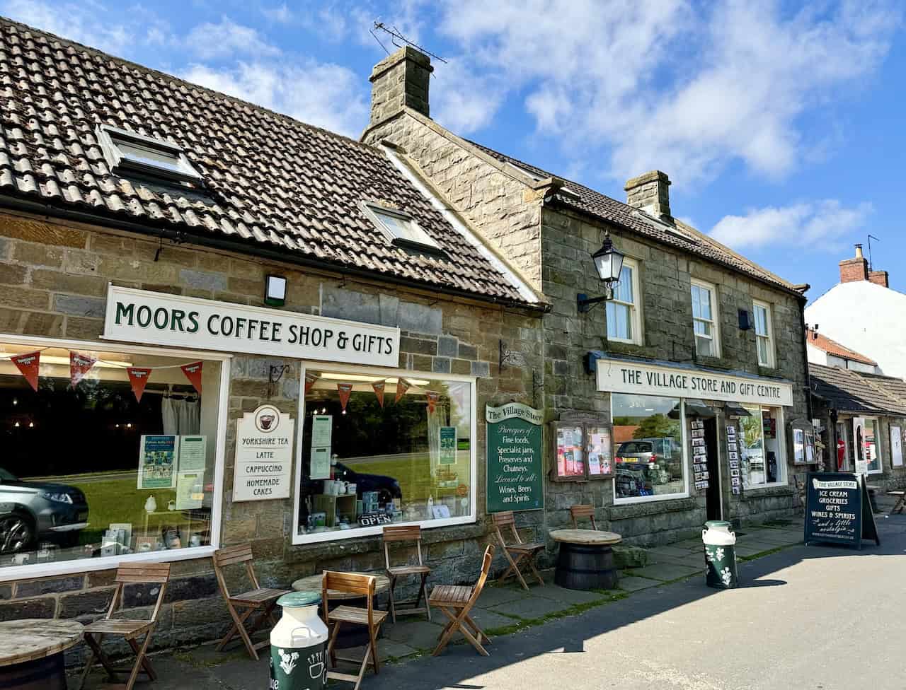 Moors Coffee Shop & Gifts and The Village Store and Gift Centre in Goathland, featuring charming stone buildings. The coffee shop serves various drinks and homemade cakes, while the village store offers fine foods and beverages.
