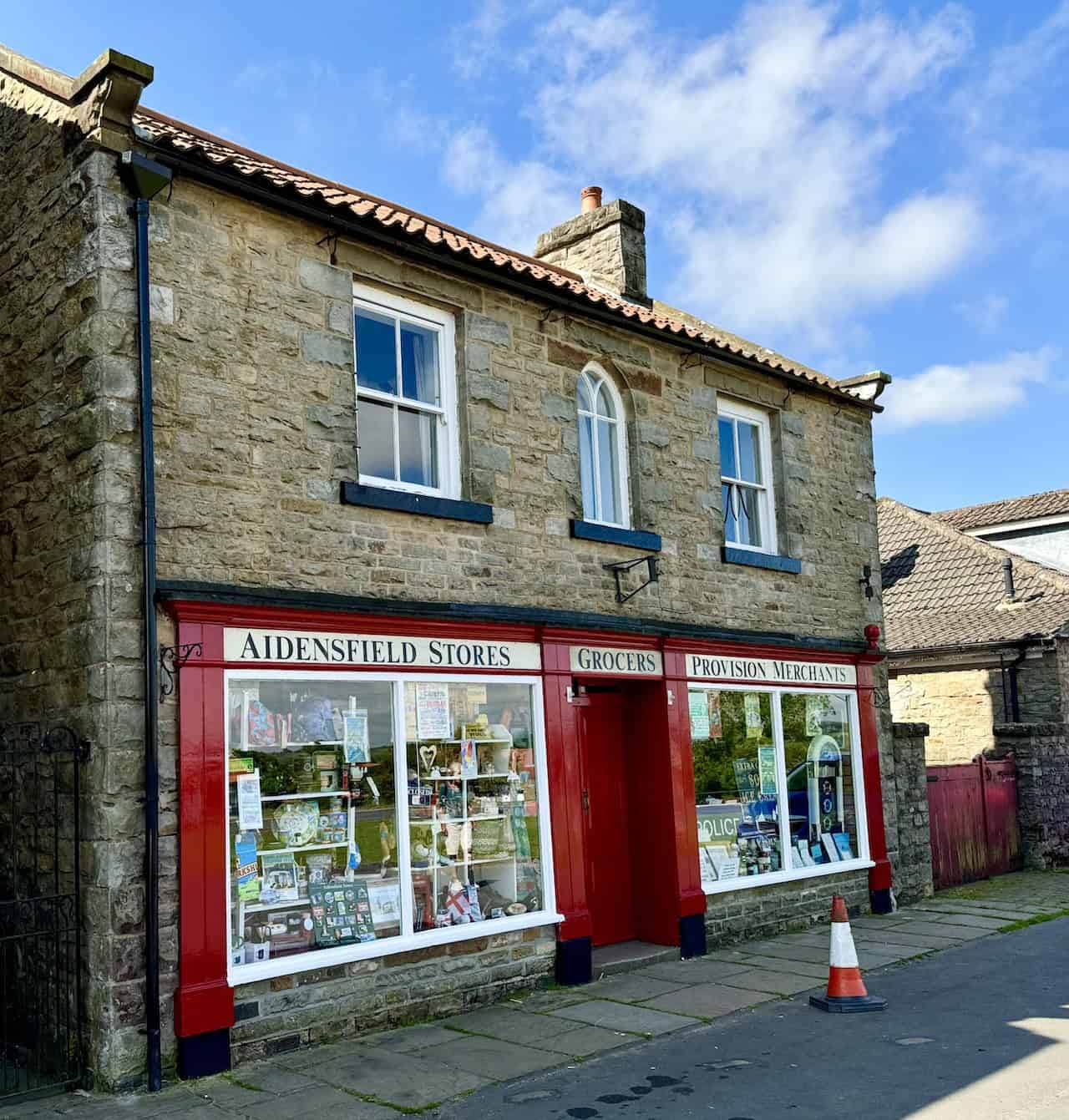 Aidensfield Stores with its distinctive red and cream exterior. Known for its role in Heartbeat, it served as the village's grocery and provision merchants, displaying memorabilia in its large windows.
