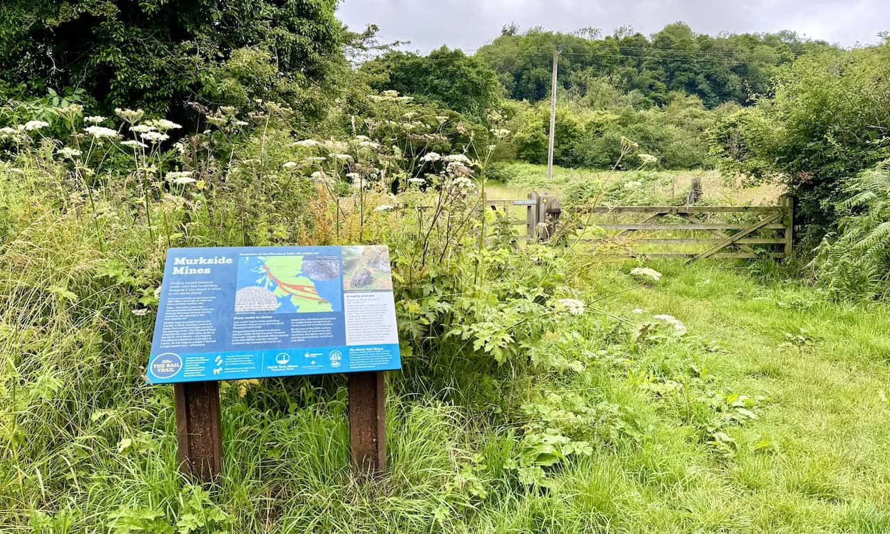 Display board containing information about Murkside Mines. Through the gate, a small detour path leads to heaps of disfigured black ironstone rock.