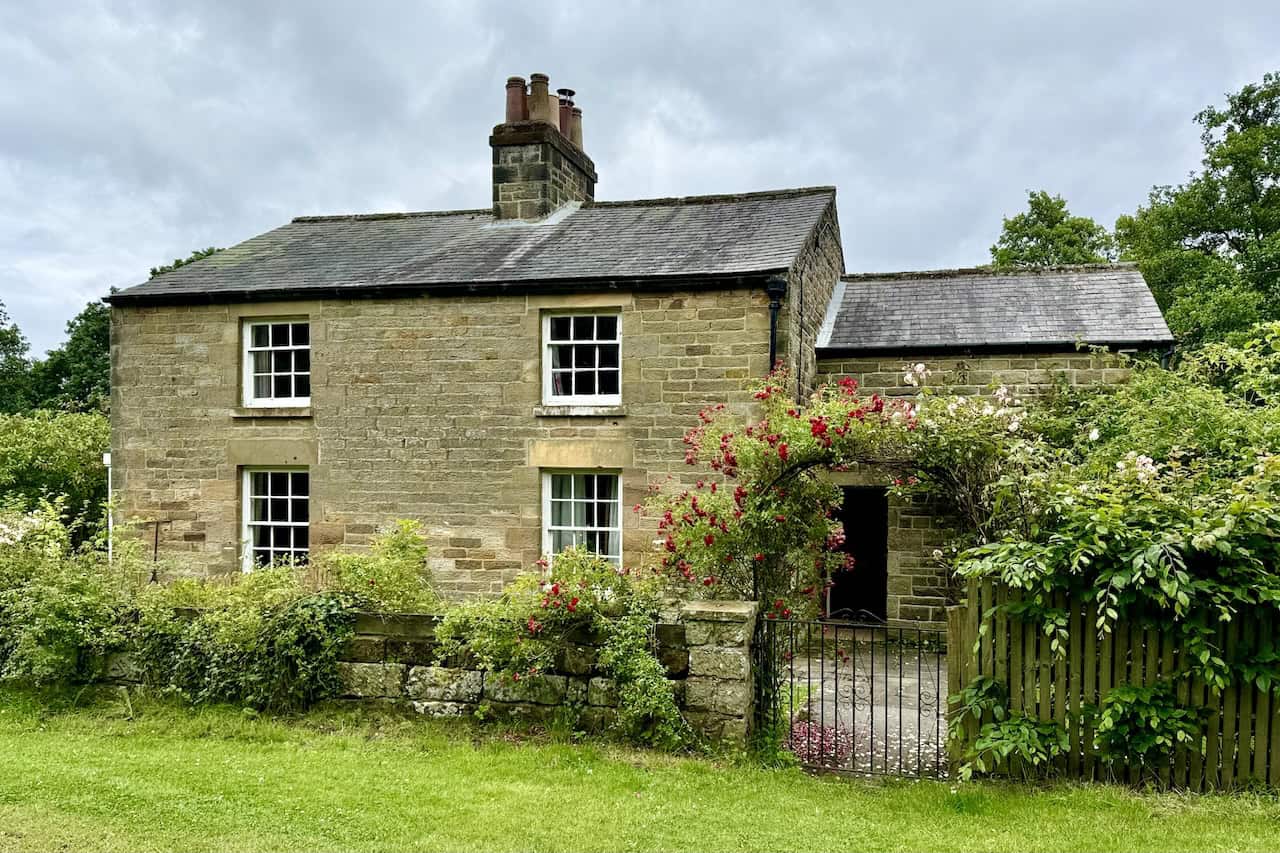 Traditional stone cottage with a slate roof by the side of the track. The arched entrance is adorned with climbing roses in full bloom, a picturesque sight on the Goathland to Grosmont walk.