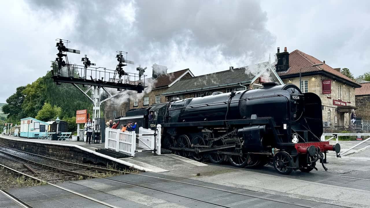 Grosmont Railway Station with a departing steam train, offering benches, a shop, a cafe, and toilet facilities for a relaxing visit.