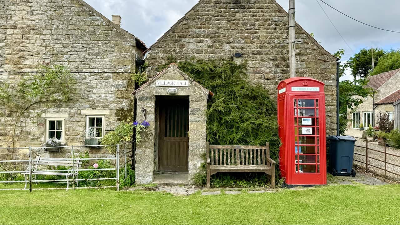 Levisham village hall with a bench for breaks or lunch, featuring a red phone box housing a defibrillator and books.