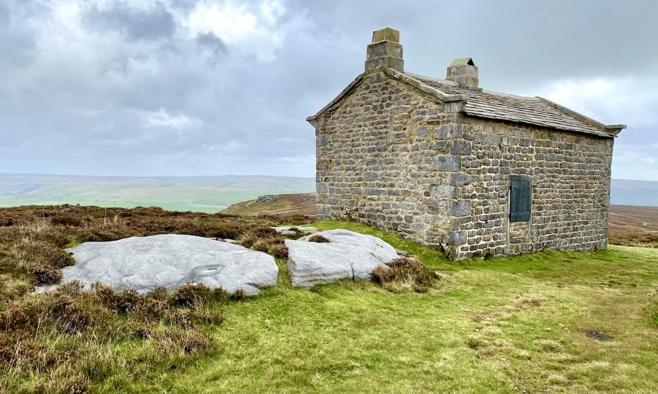 Solitary stone grouse shooting hut beside the track across Burnsall and Thorpe Fell, constructed from rough-hewn stone with a slate roof in a remote moorland setting.