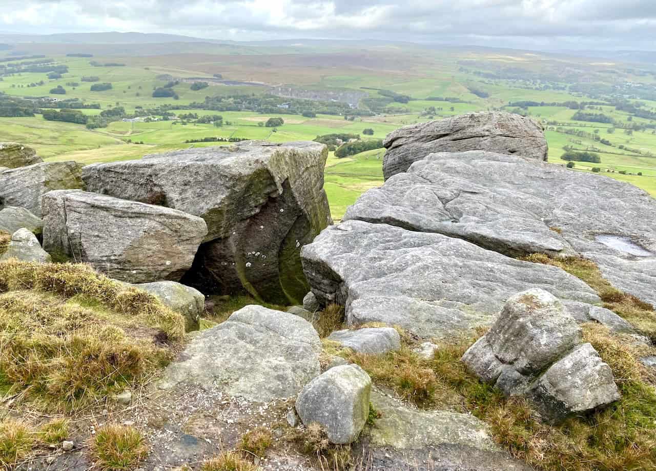 Rolling Gate Crags, a rugged outcrop of large, weathered rocks on the hillside, with a wide green valley, Cracoe village, and Swinden Quarry visible in the background.