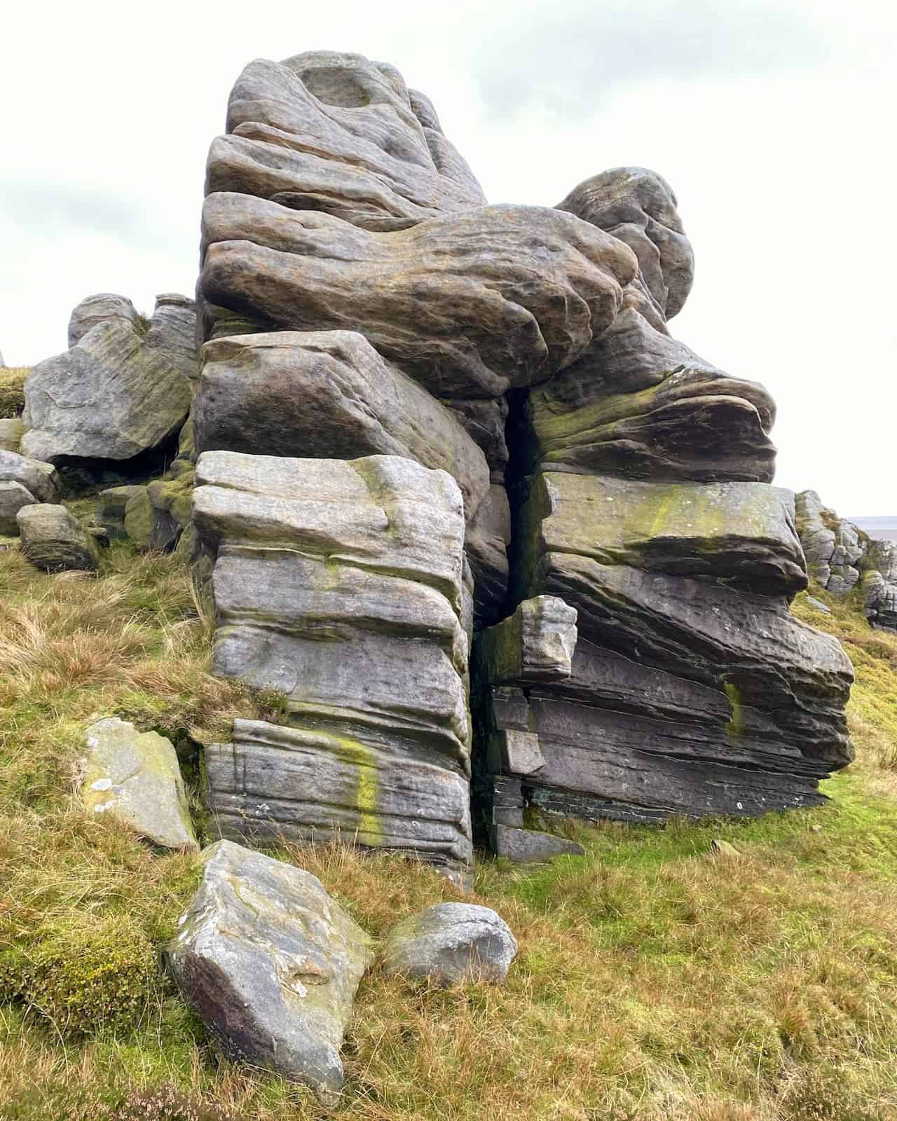 Weathered gritstone formations with deep grooves and cracks, contrasting against the surrounding grass and moorland vegetation.