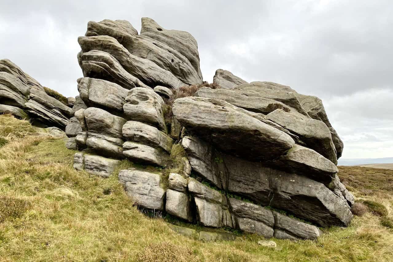 Weathered gritstone formations with deep grooves and cracks, contrasting against the surrounding grass and moorland vegetation.