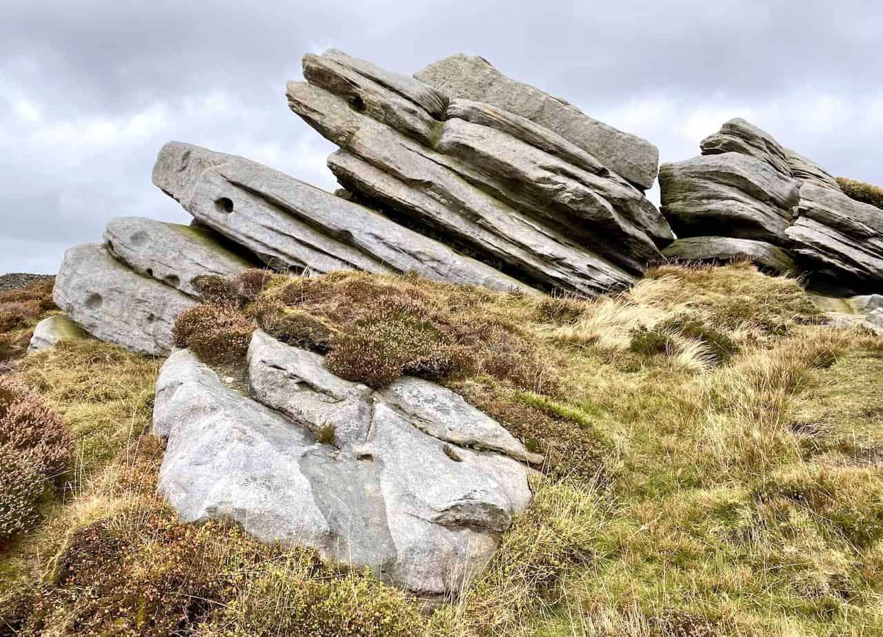 Weathered gritstone formations with deep grooves and cracks, contrasting against the surrounding grass and moorland vegetation.