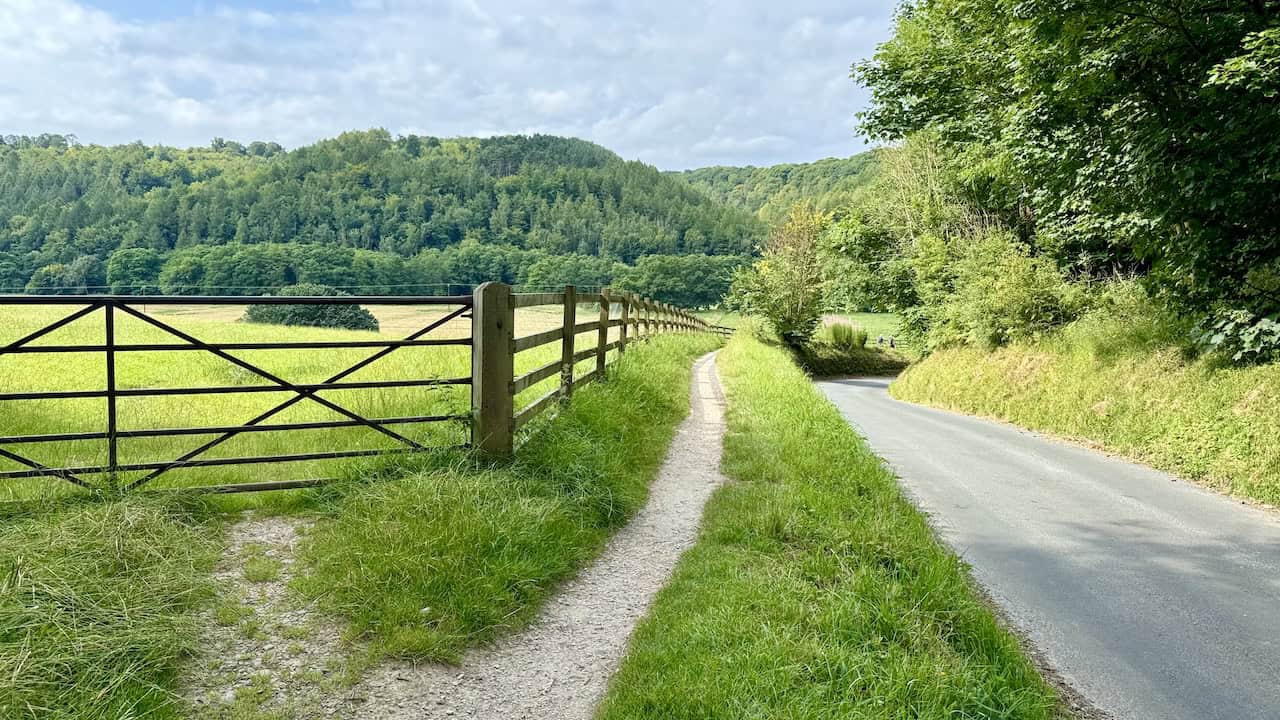 A tarmac road with a narrow footpath on the left side, disappearing around a bend.
