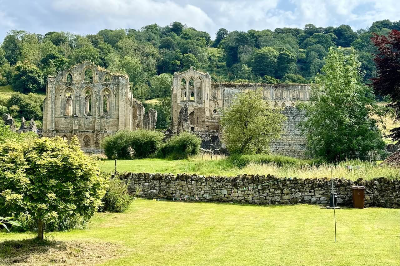 A broader view of Rievaulx Abbey, set against lush trees and hills, near the abbey's visitor centre.
