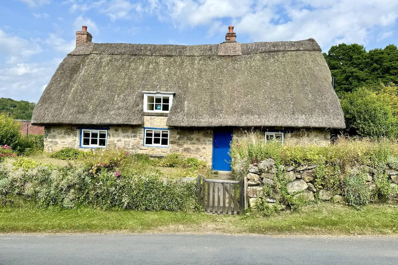 A traditional English cottage with a thatched roof, located along the road past the abbey.
