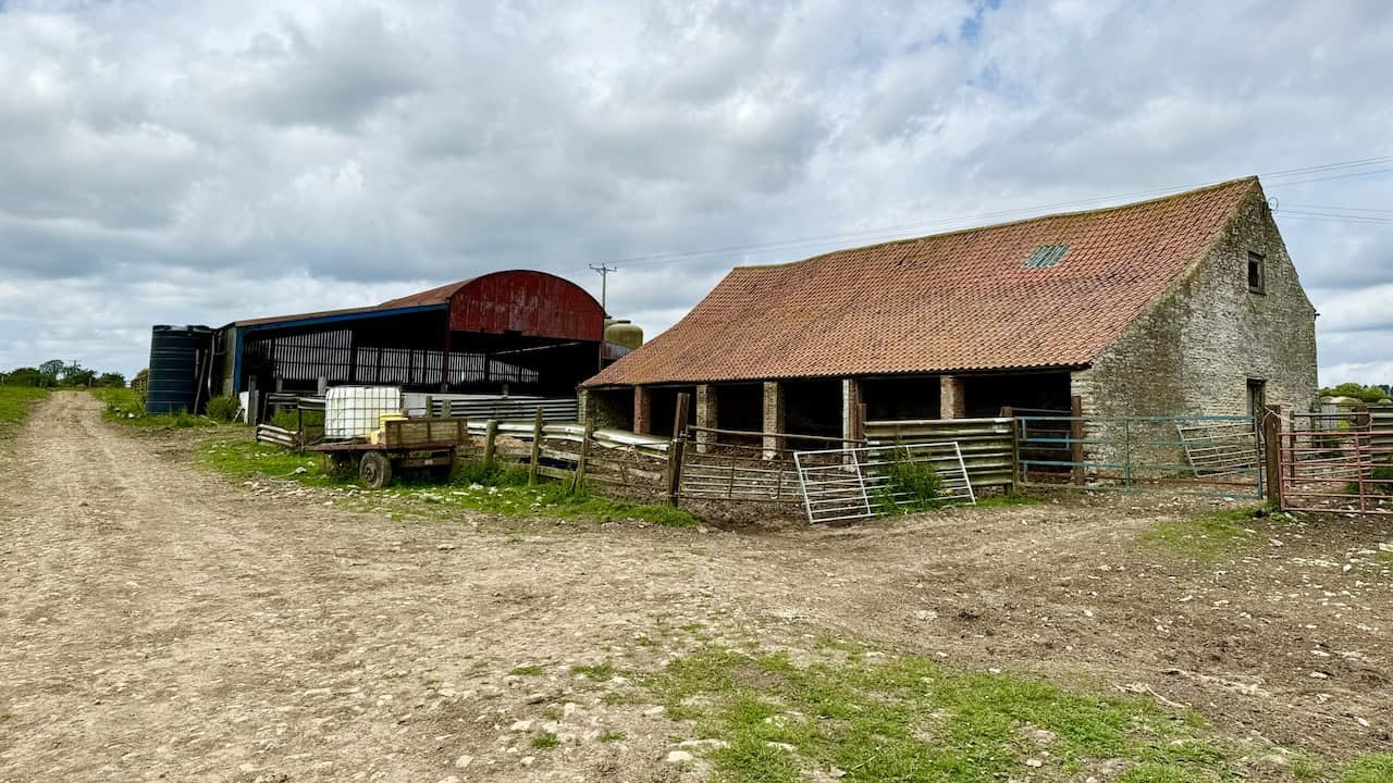 Tylas Barn with the route continuing past the left side of farm buildings, heading west.
