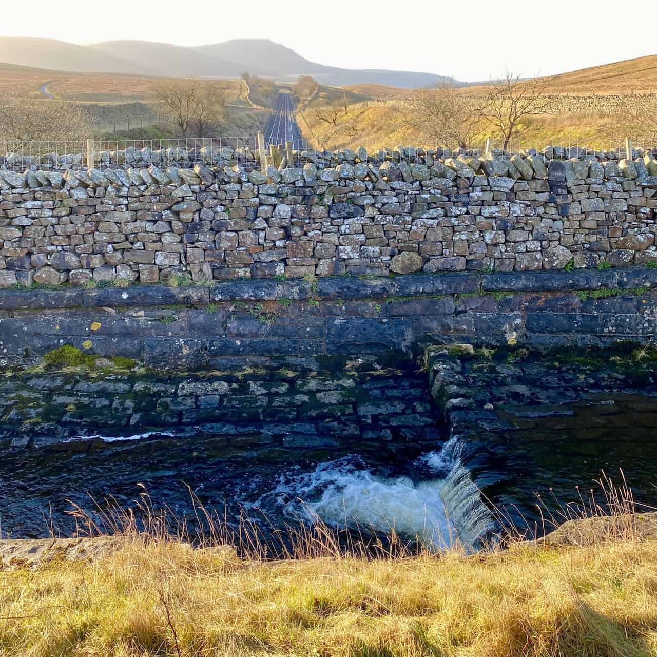 Scenic view looking south from the Little Dale aqueduct, where the Settle to Carlisle Railway aligns with the silhouette of Ingleborough in the distance.